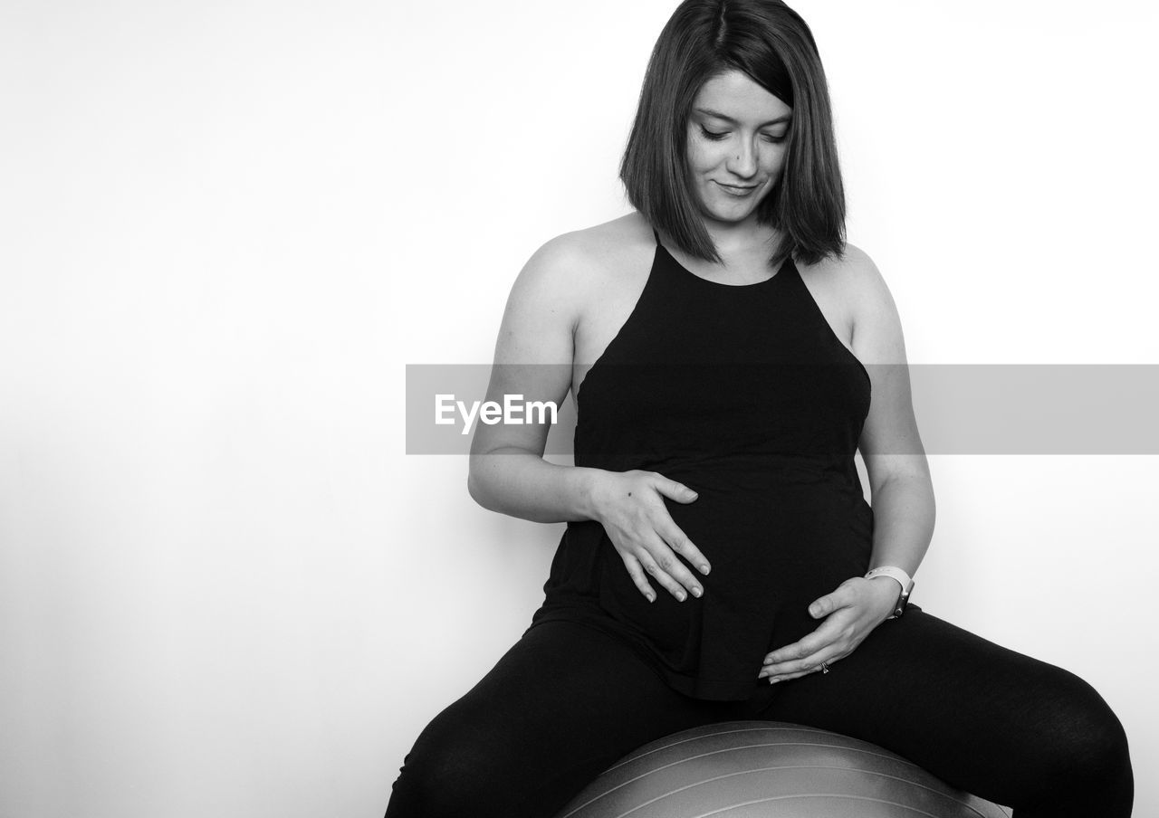 Smiling pregnant woman sitting on fitness ball against white background