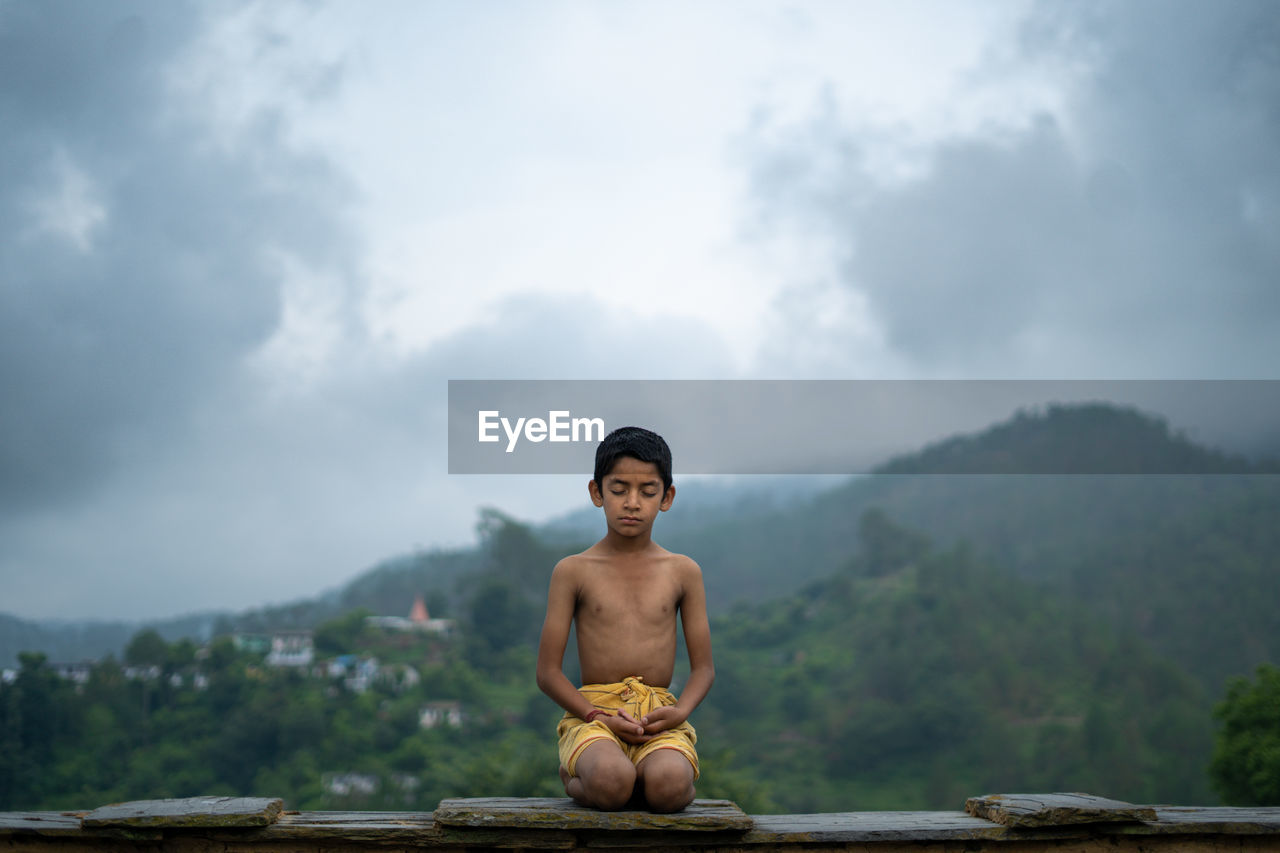 A young indian cute kid doing yoga in the mountains,wearing a dhoti