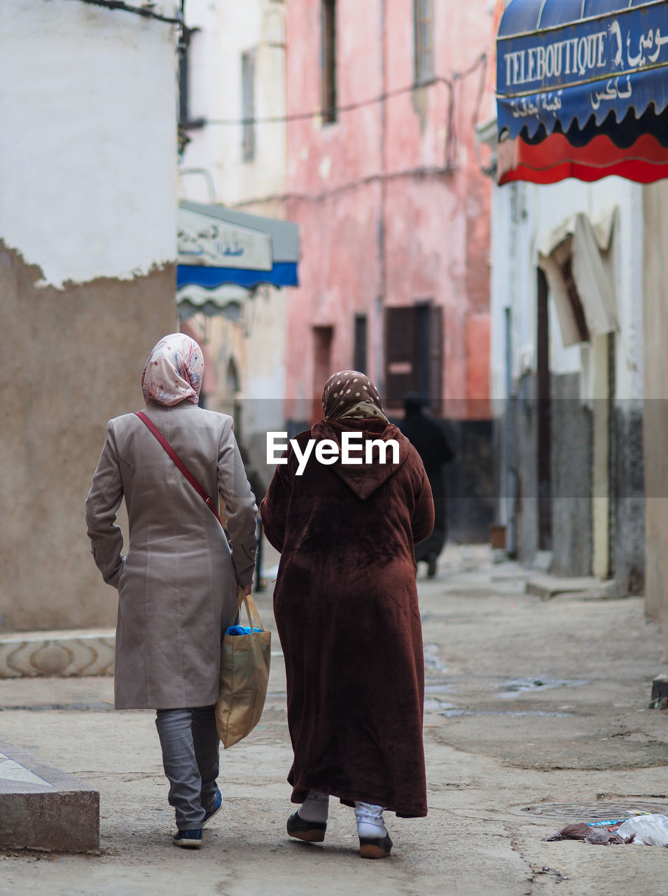 REAR VIEW OF WOMAN WALKING ON STREET AGAINST BUILDING