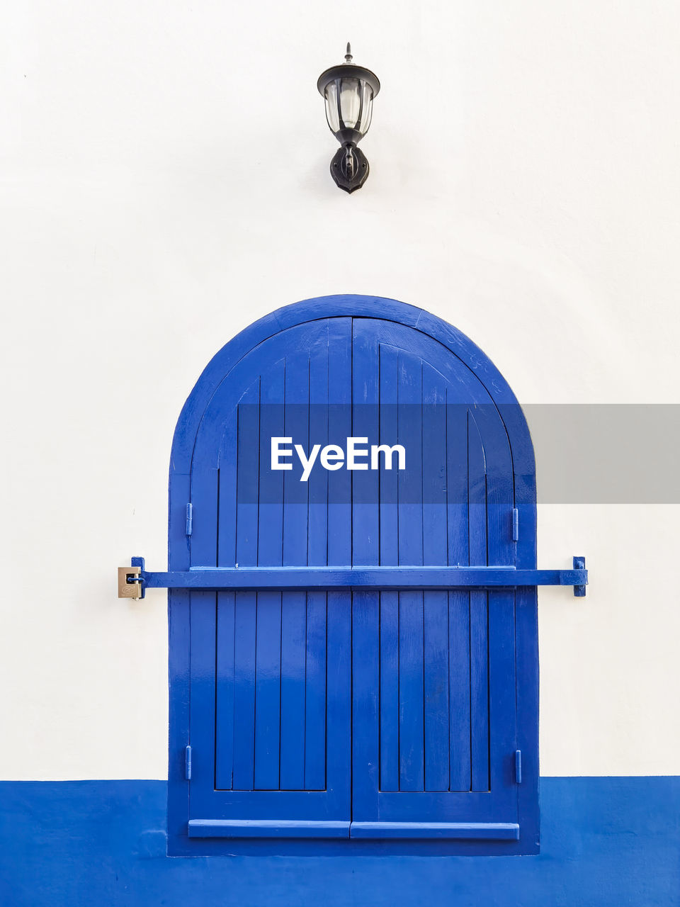 Simple blue locked window with a traditional lamp above in the streets of asilah