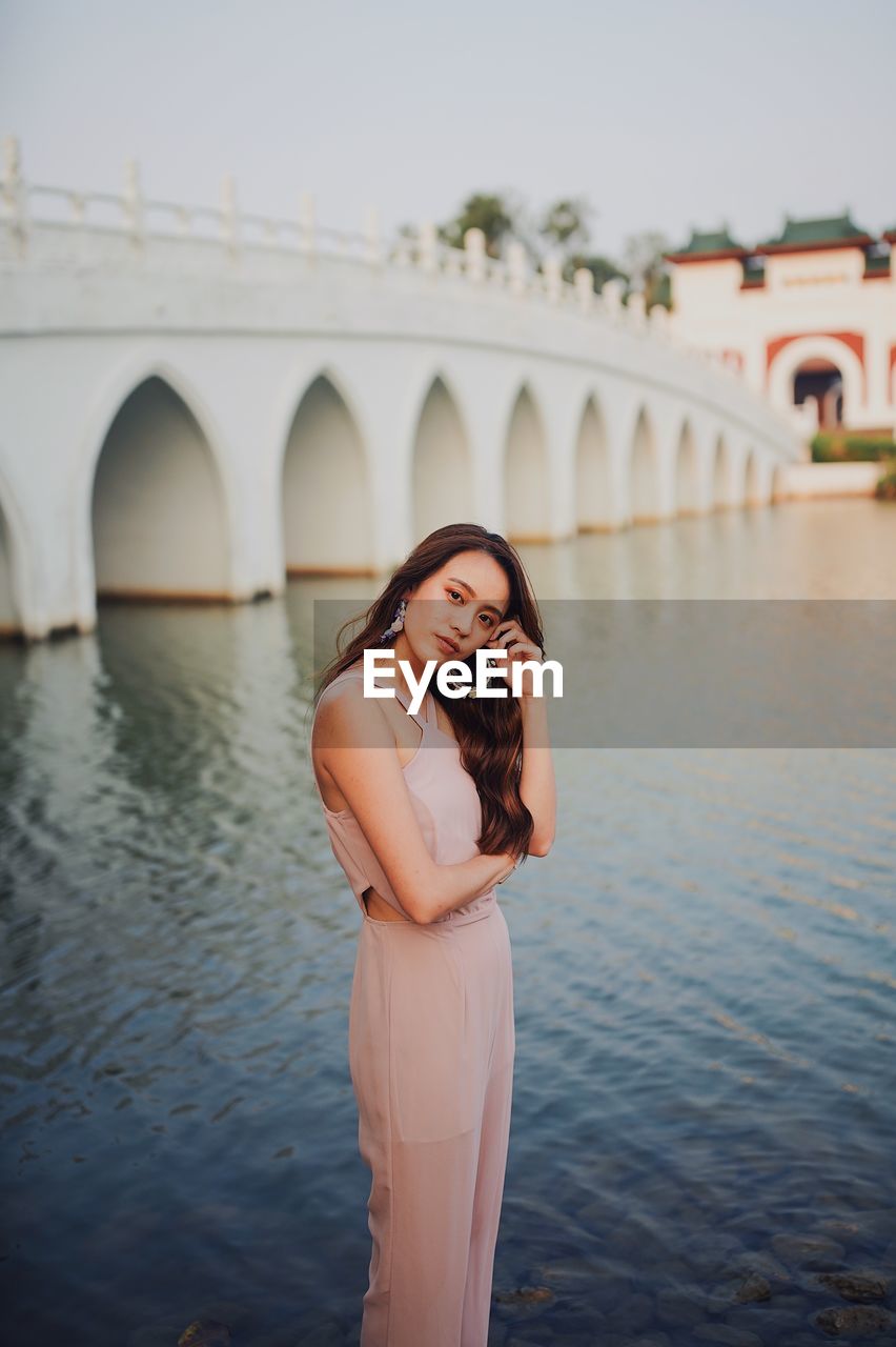 Young woman standing against bridge over water