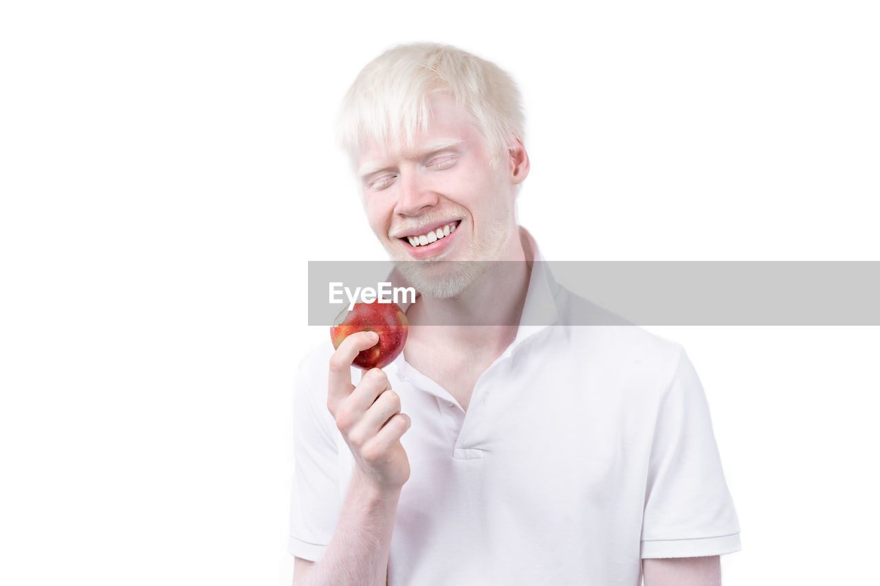 MID ADULT MAN EATING APPLE AGAINST WHITE BACKGROUND