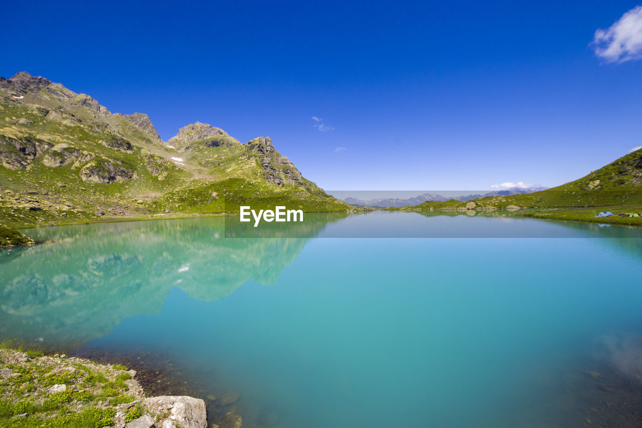 Scenic view of lake and mountains against clear blue sky