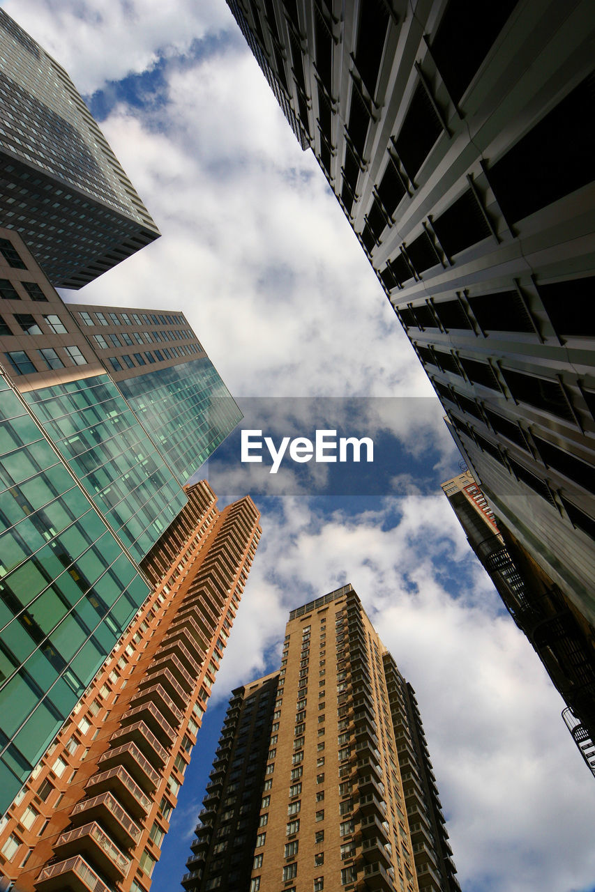 Low angle view of modern buildings against cloudy sky in city