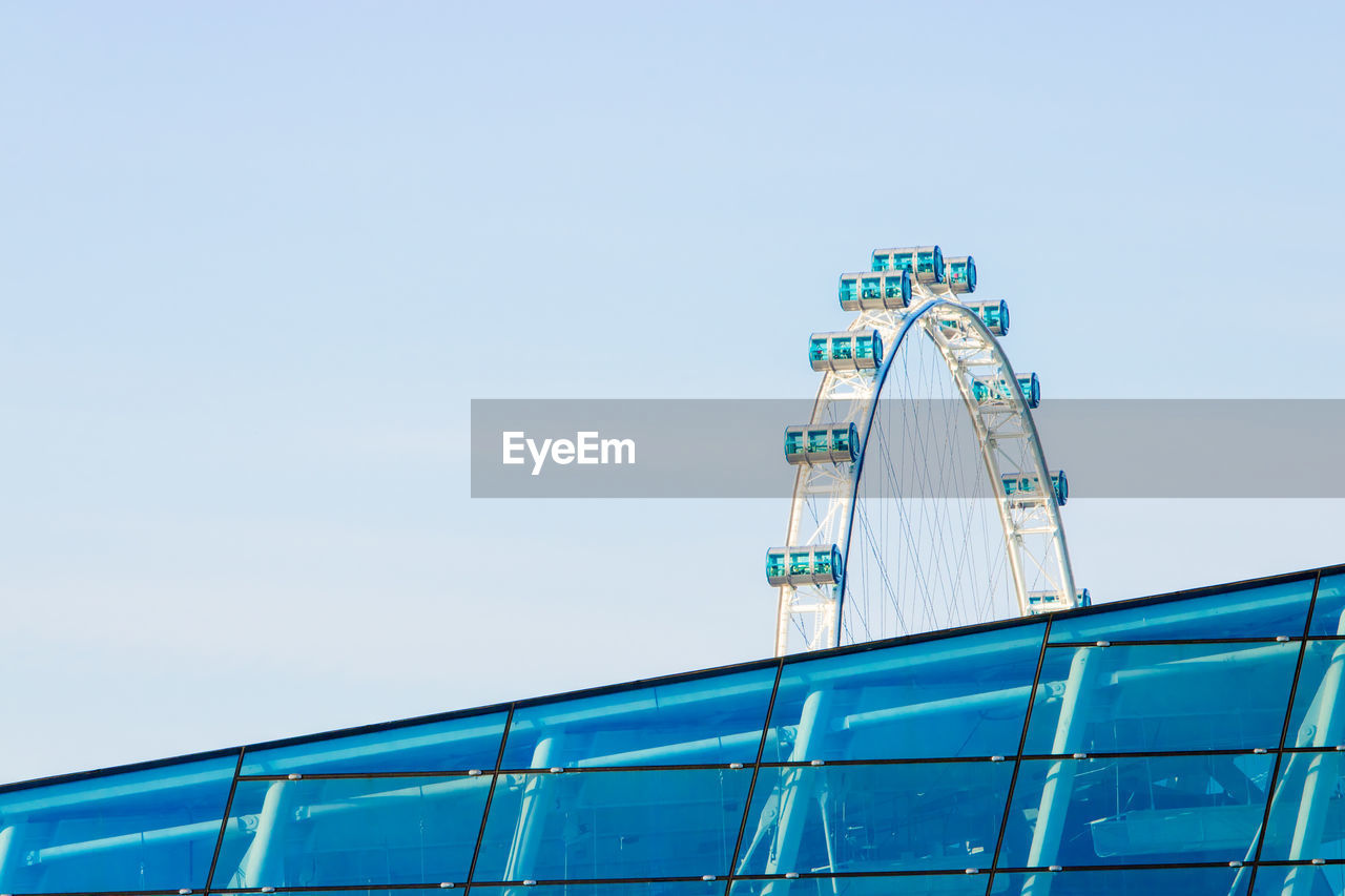 Low angle view of singapore flyer behind glass building