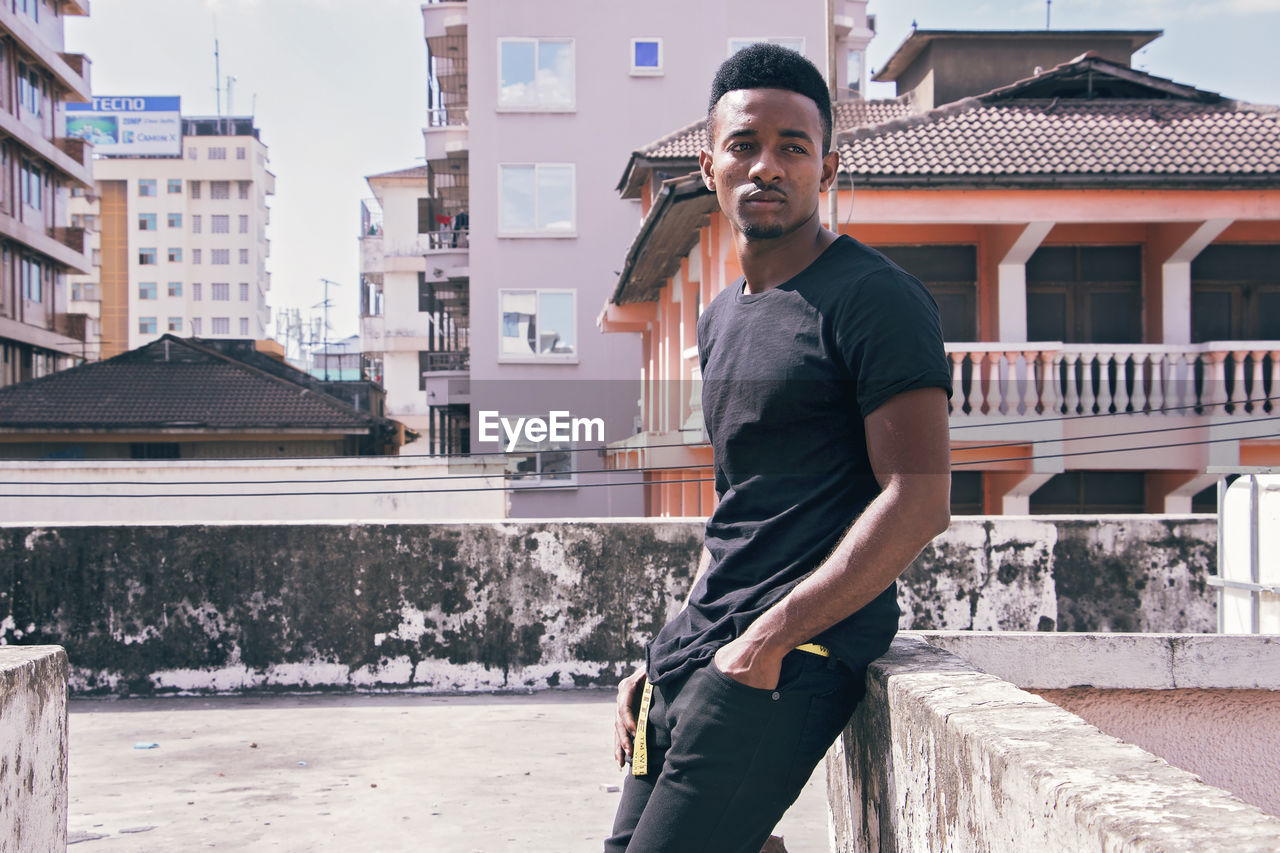 Young man looking away while standing against building 