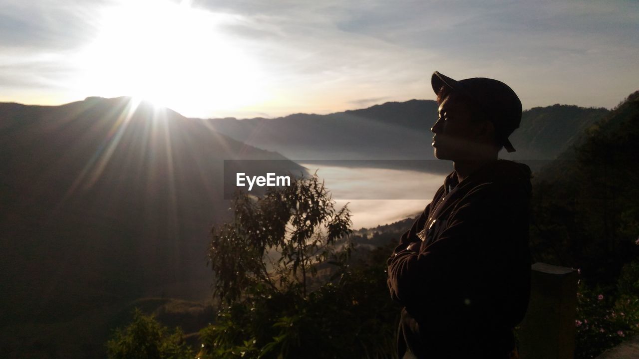 MAN STANDING ON MOUNTAIN AGAINST SKY