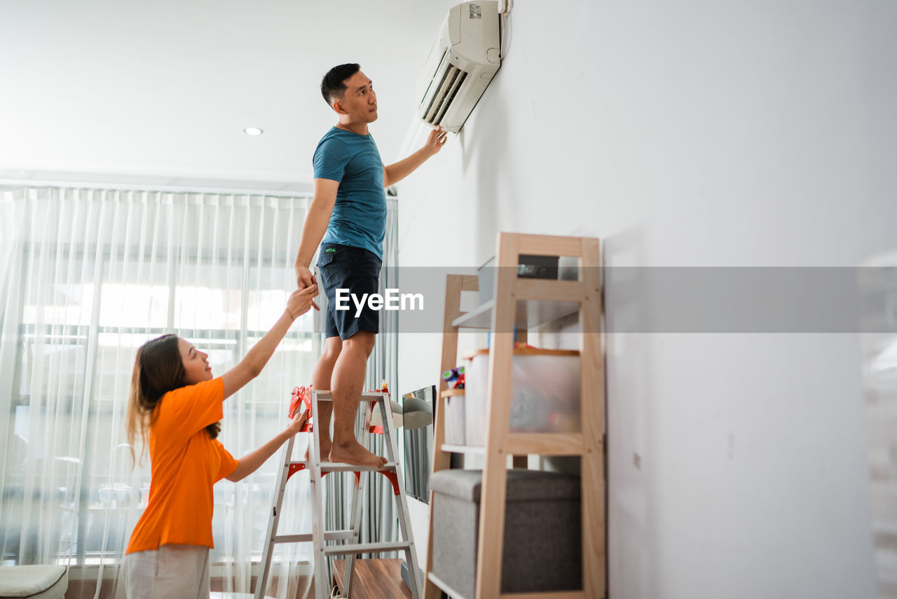 side view of man playing with arms raised standing against wall