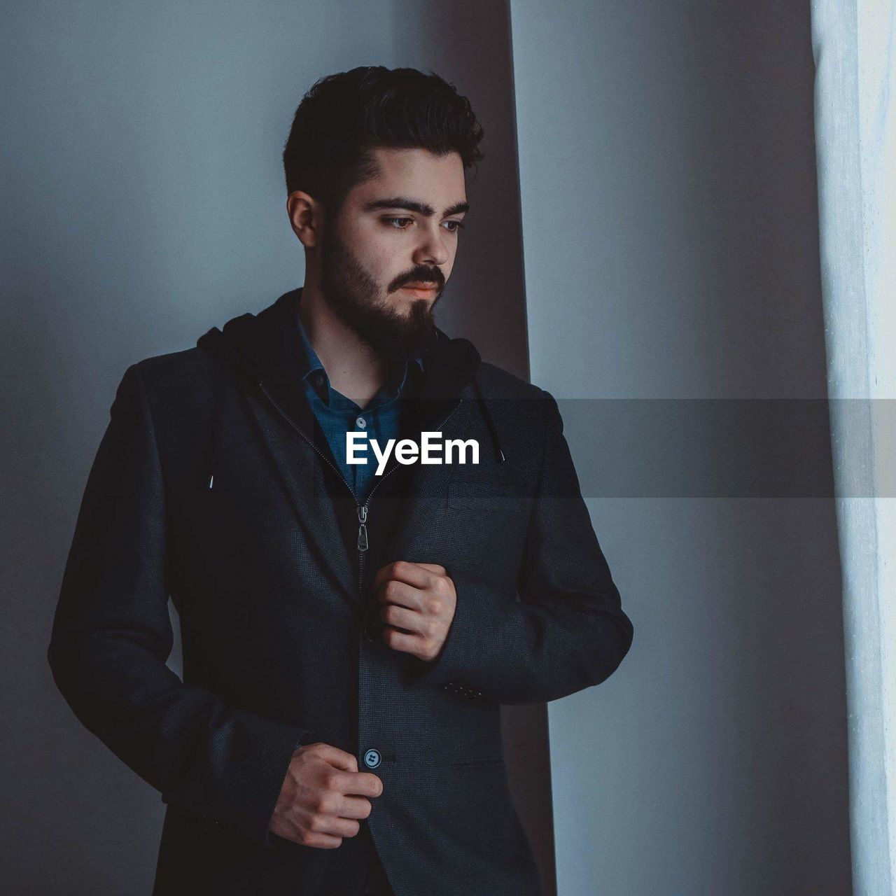 Thoughtful young man wearing coat standing against wall