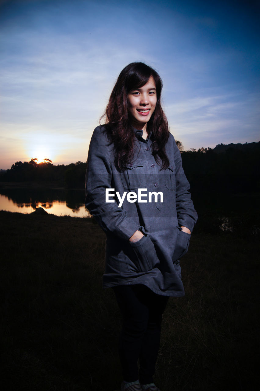 Portrait of smiling young woman standing on field against sky