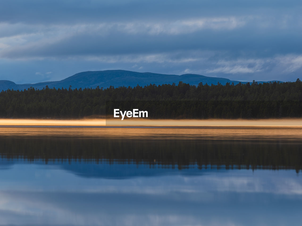 A tranquil dawn illuminates a lake in norway, its reflection shimmering beneath the morning mist. 