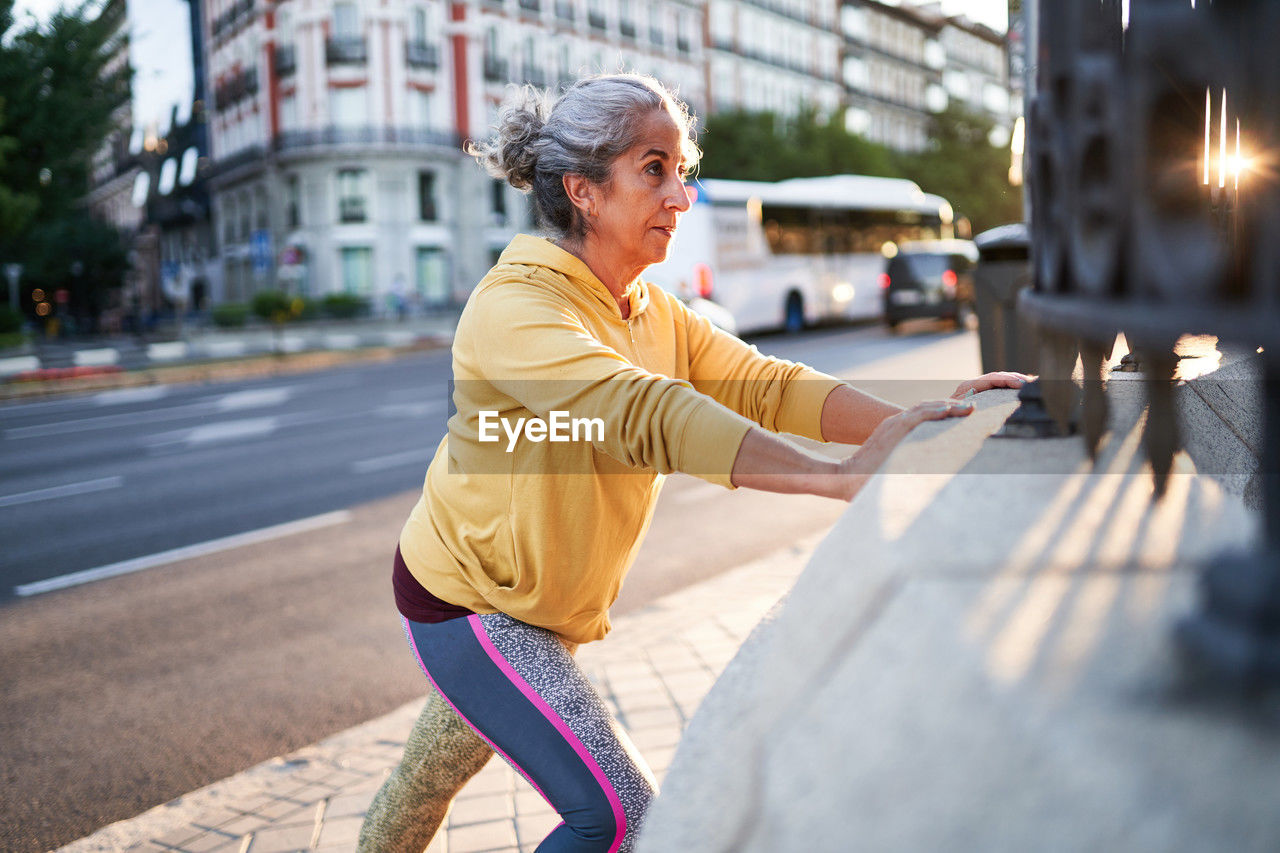 Elderly female athlete smiling and doing push ups near park fence during fitness workout in morning on street