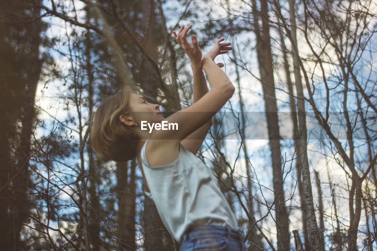 Low angle view of young woman dancing in forest