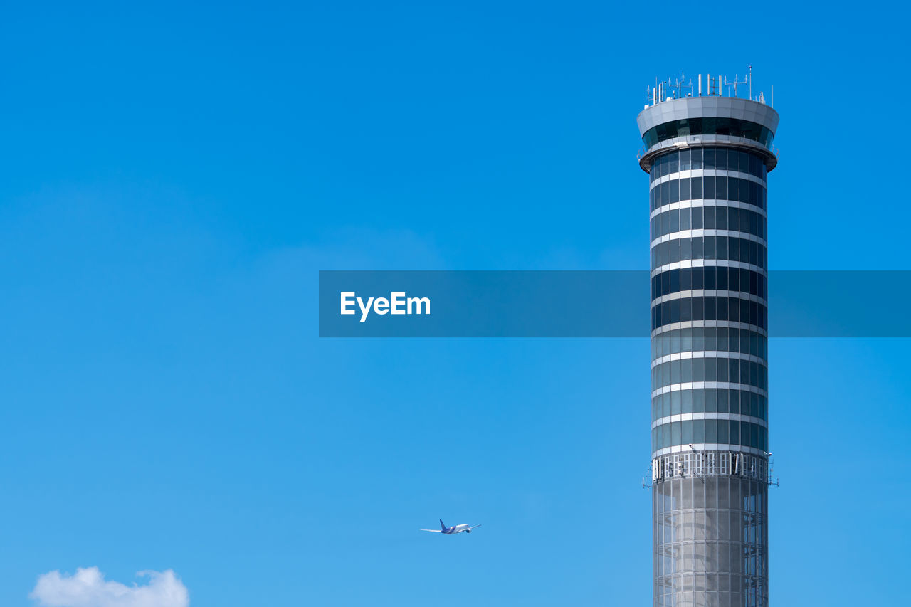 Air traffic control tower in the airport with international flight plane flying on clear blue sky.