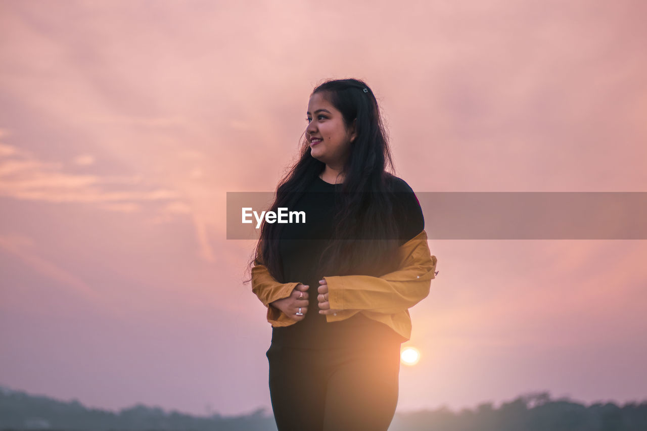 WOMAN STANDING AGAINST ORANGE SKY