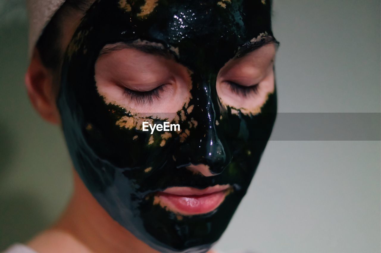 Young woman with eyes closed in facial mask against wall