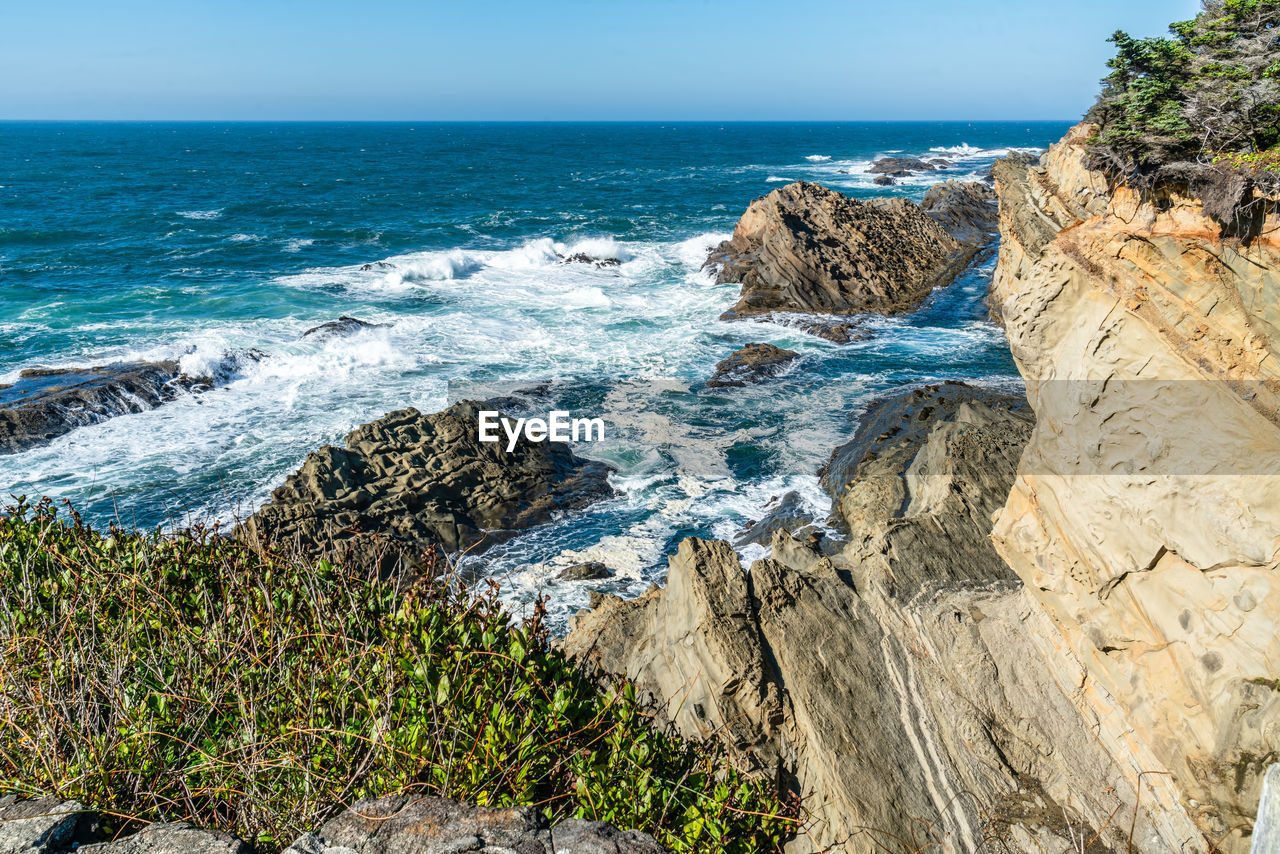 sea, water, land, beach, rock, beauty in nature, scenics - nature, shore, cliff, horizon over water, sky, coast, nature, horizon, body of water, ocean, wave, vacation, terrain, no people, day, motion, tranquility, tranquil scene, rock formation, blue, outdoors, sports, travel destinations, cove, idyllic, coastline, water sports, travel, non-urban scene, clear sky, bay, plant, environment, sunlight