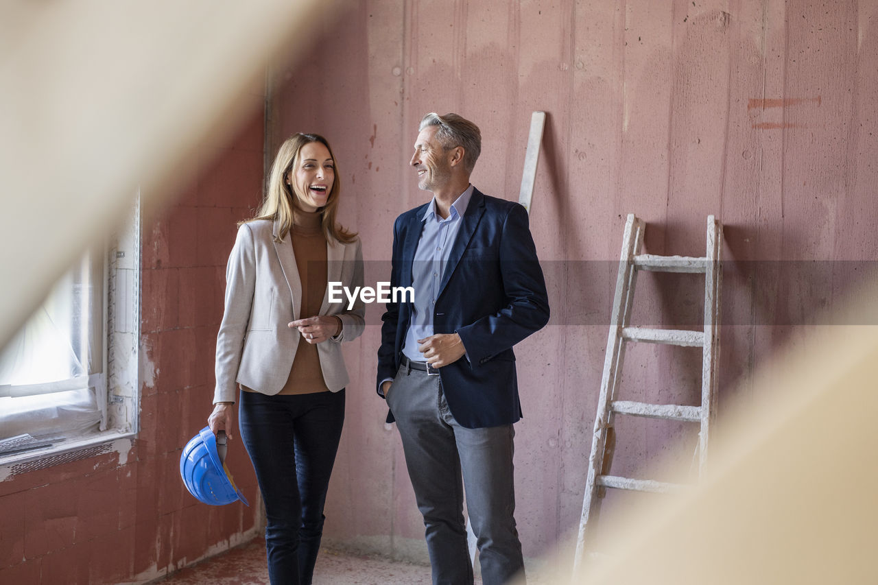 Smiling female colleague discussing with male architect at construction site