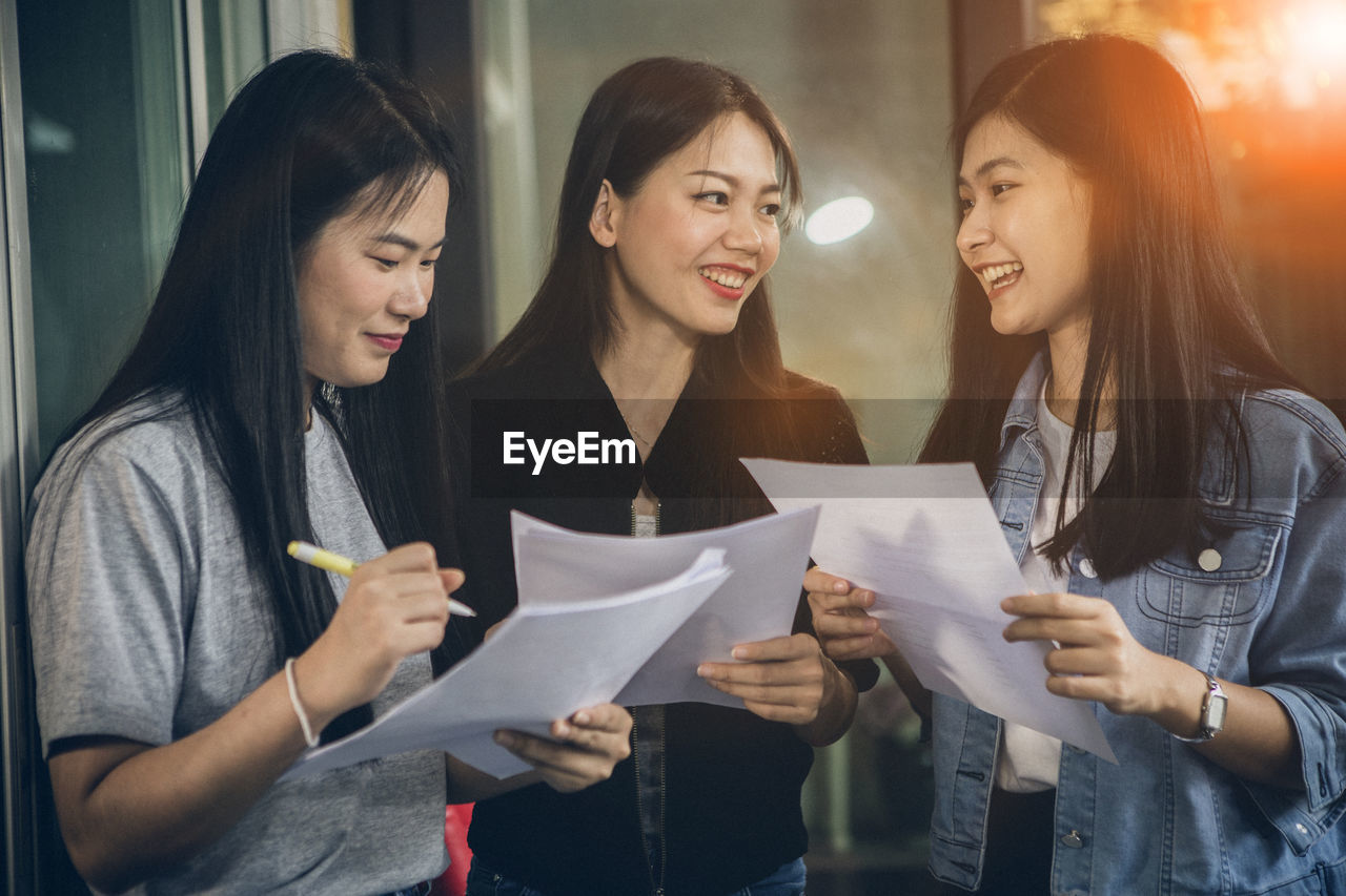 Cheerful colleagues holding papers while standing at office