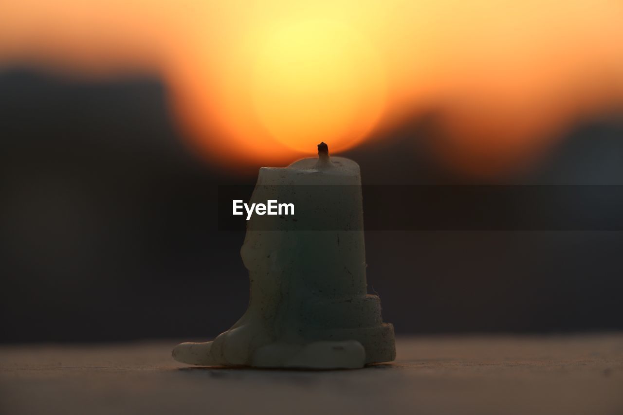 Close-up of wax candle against orange sky during sunset