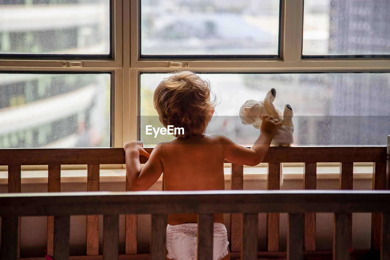 Rear view of shirtless boy looking through window