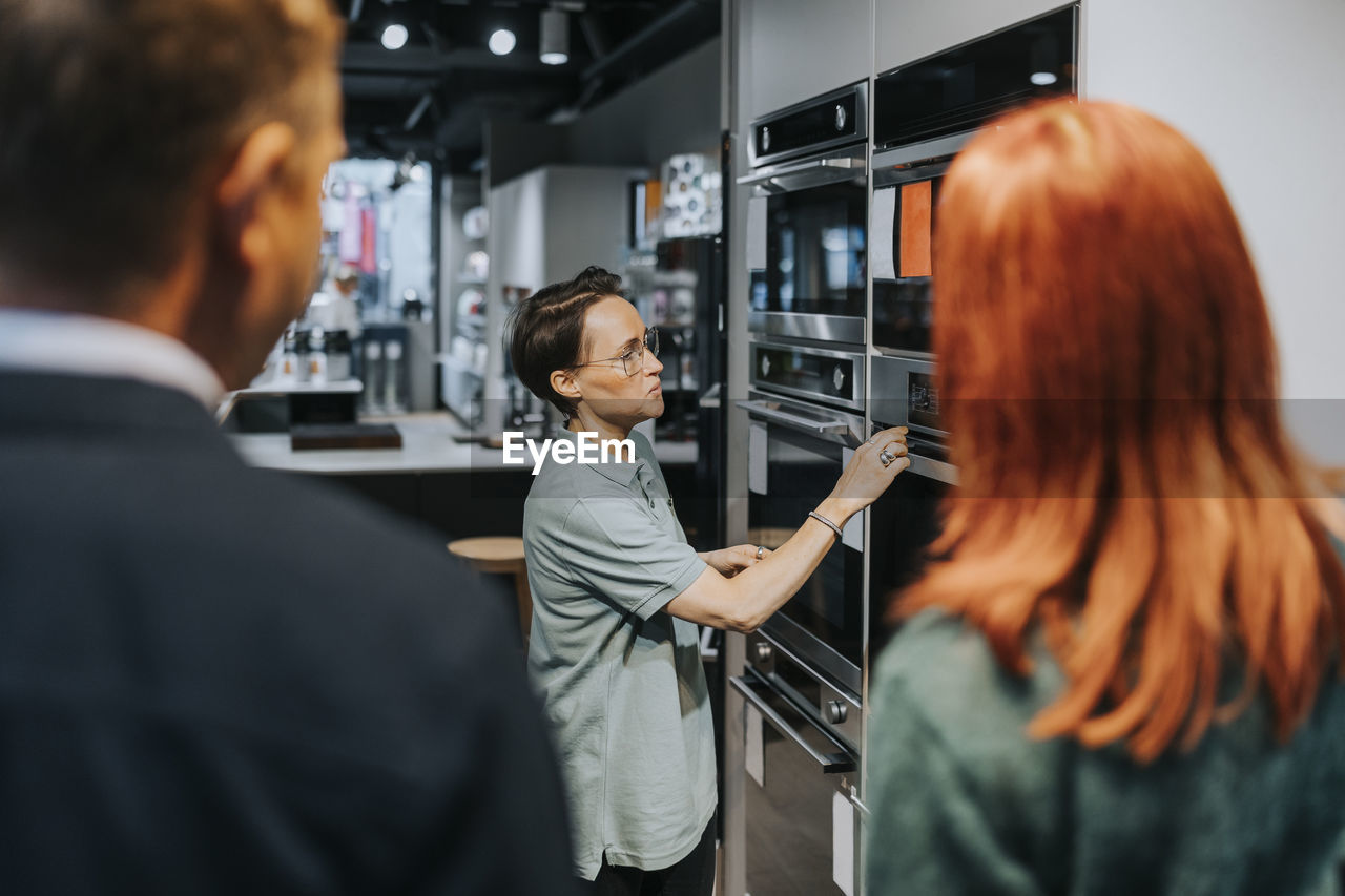 Side view of saleswoman assisting couple in buying microwave oven at electronics store