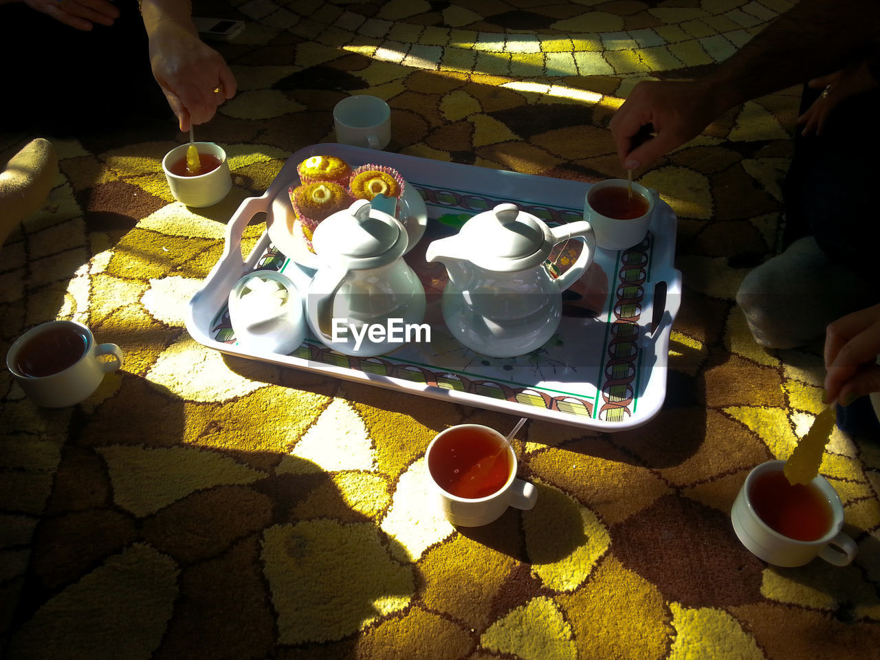 human hand, food and drink, tea cup, human body part, real people, cup, tea - hot drink, teapot, shadow, coffee cup, sunlight, holding, food, plate, refreshment, drink, table, coffee - drink, saucer, high angle view, bowl, day, men, women, sitting, lifestyles, dessert, freshness, outdoors, tray, close-up, ready-to-eat, people, adult