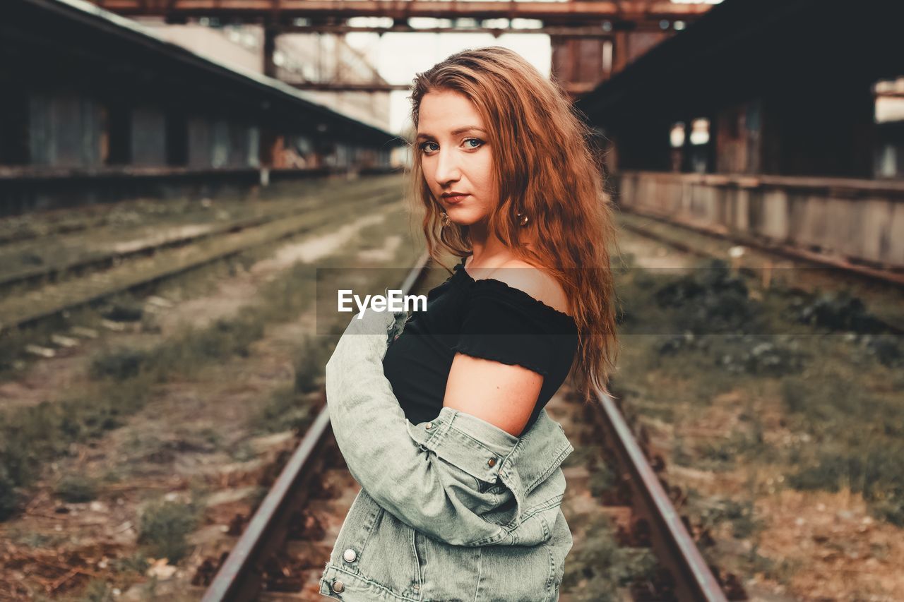 Portrait of beautiful woman standing on railroad track