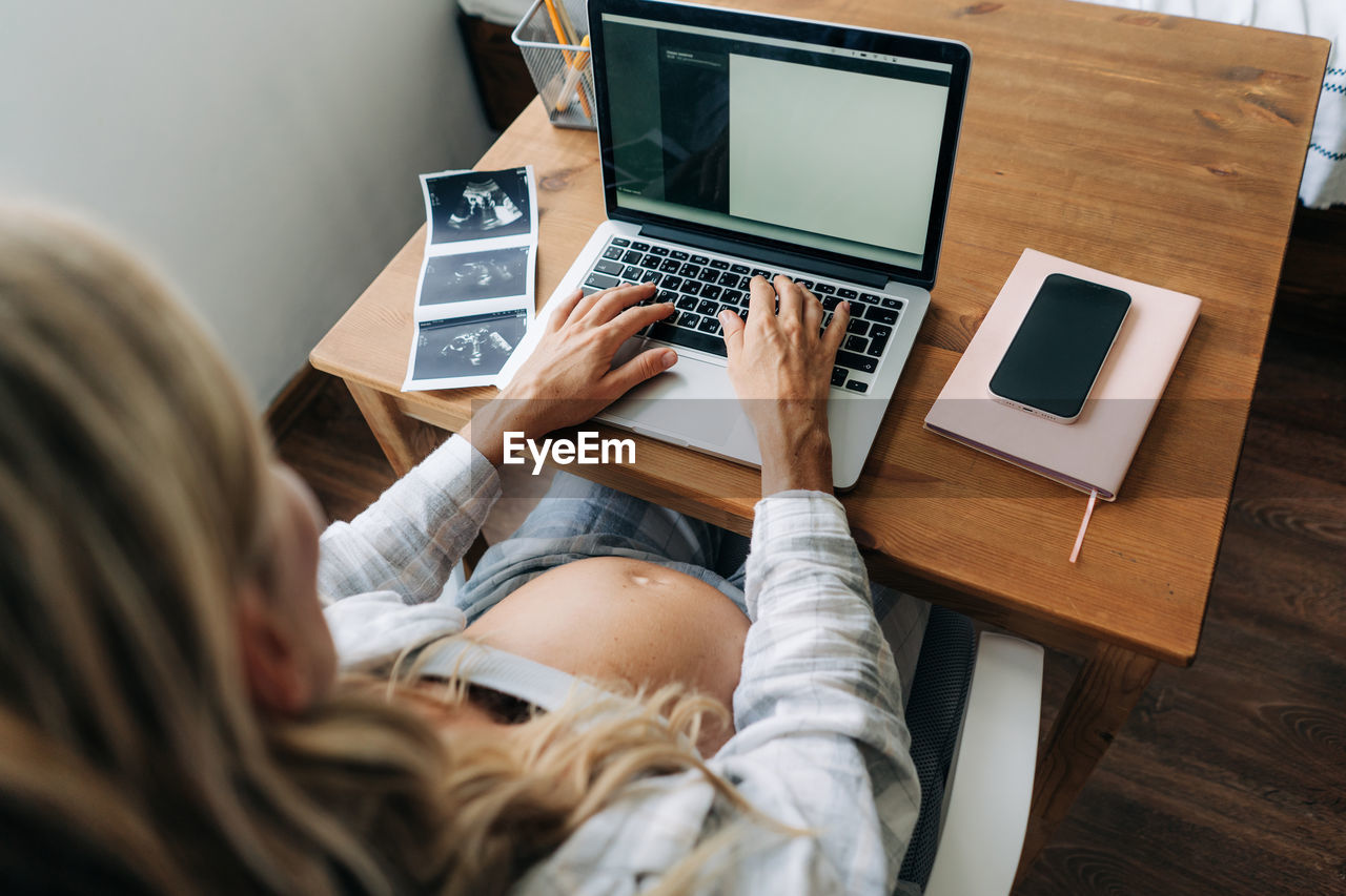 Unrecognizable pregnant woman typing perinatal notes in notes on computer.