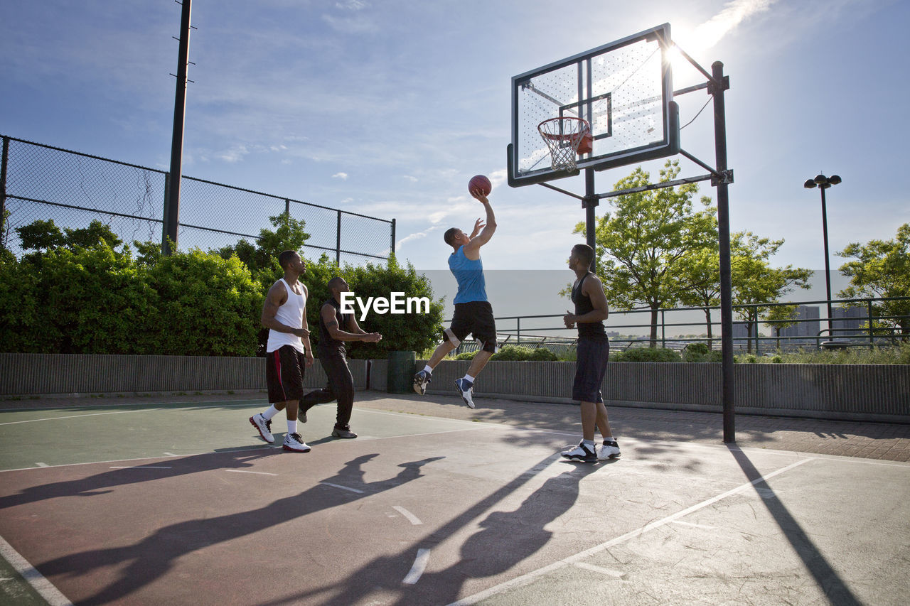 Friends playing basketball in court on sunny day