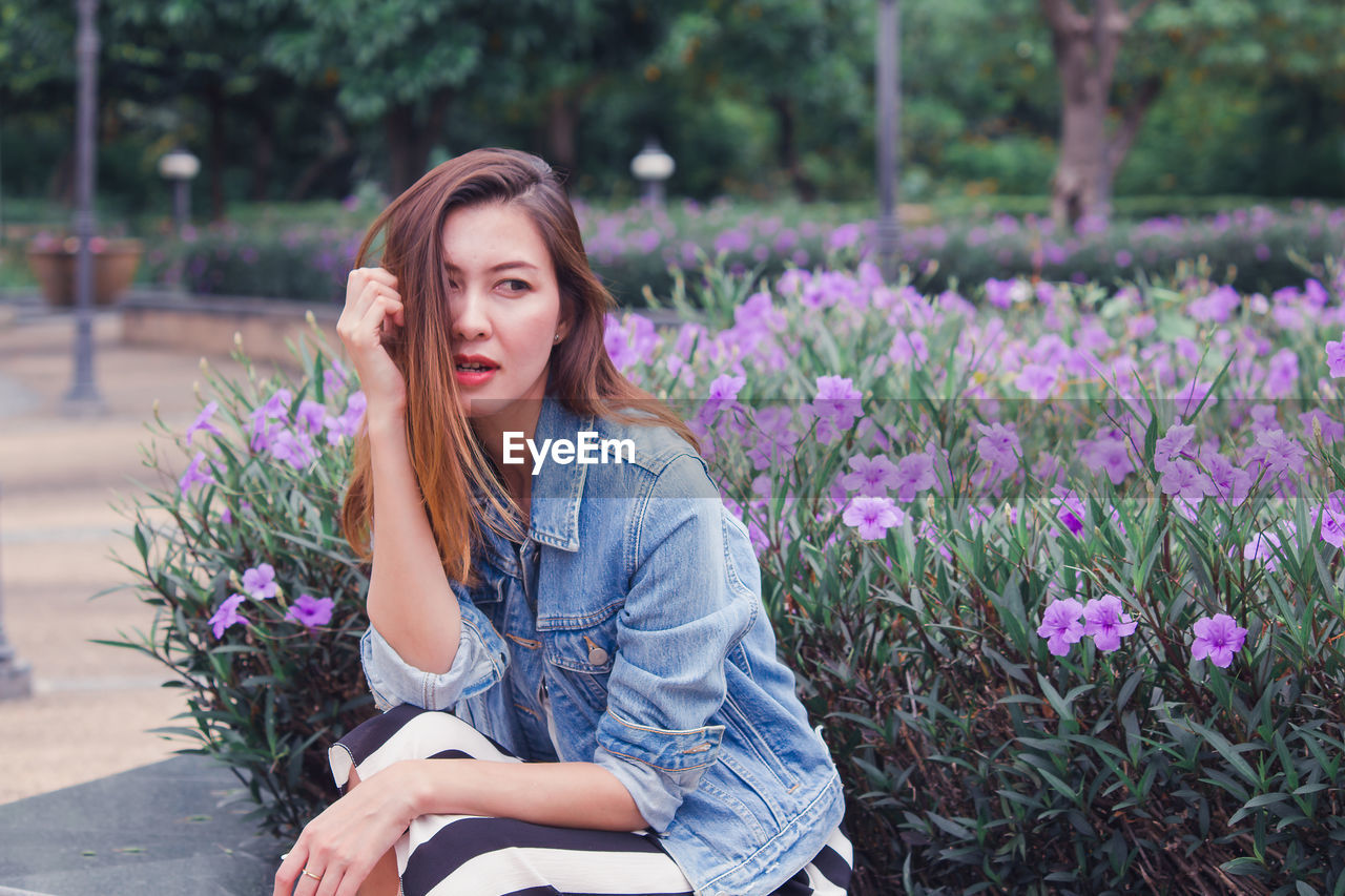 YOUNG WOMAN SITTING ON PURPLE FLOWERING PLANTS