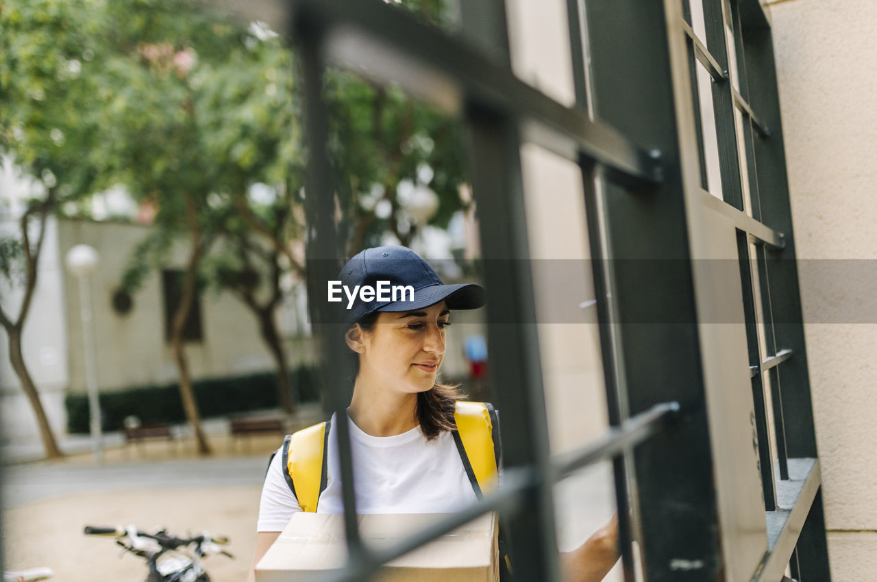 Female delivery person holding package while standing at gate