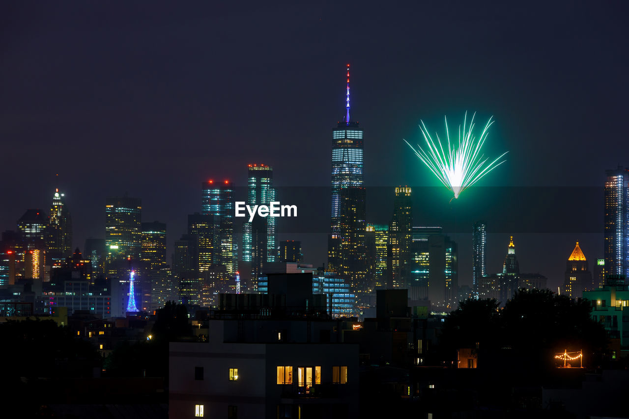 Illuminated buildings and firework display against sky at night