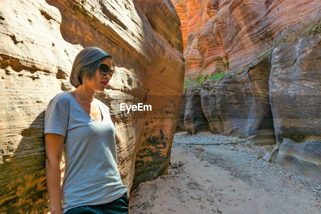 Woman wearing sunglasses standing by rock formation