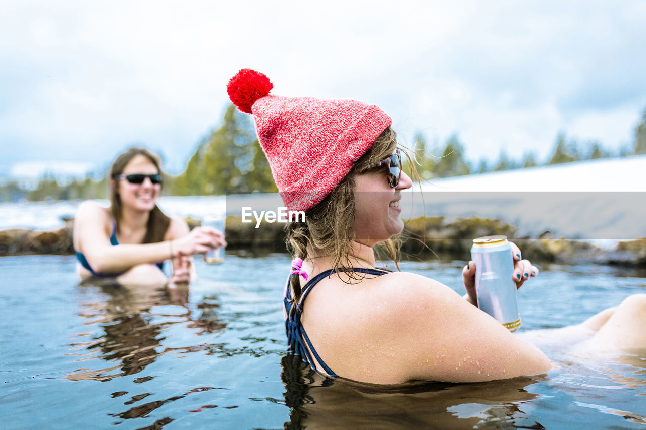 Happy female friends enjoying drinks in lake during winter