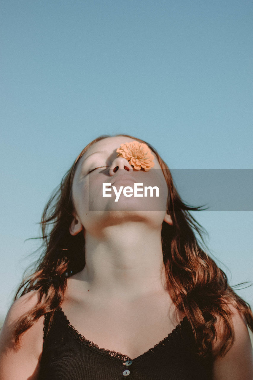 Low angle view of woman with flower on one eye against clear sky