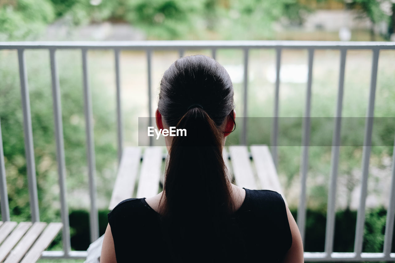 Rear view of woman with ponytail sitting at balcony