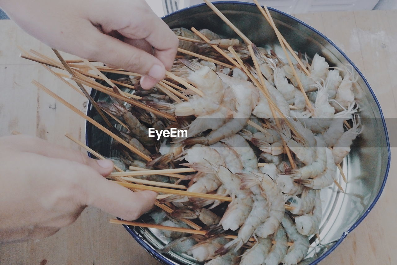 Close-up of hands holding shrimps with skewers in bucket
