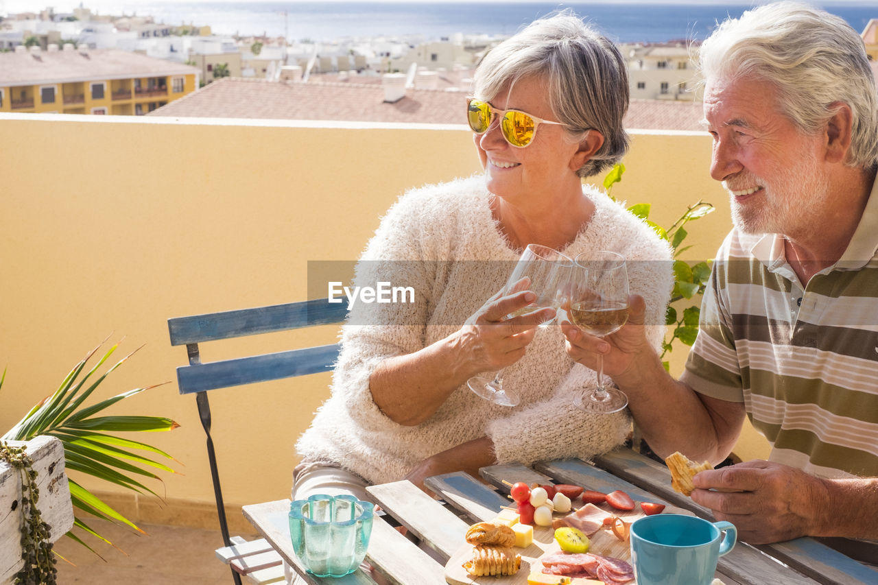 Senior couple toasting drinks while sitting in balcony