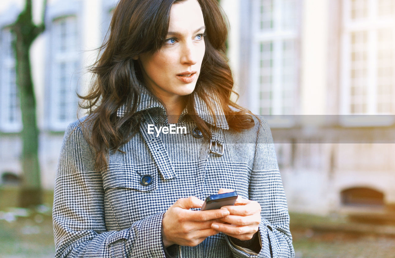 Close-up of woman using smart phone while standing against building