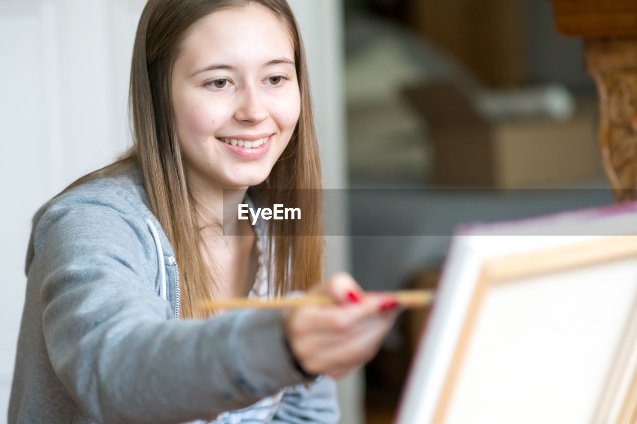 Smiling young woman painting on canvas