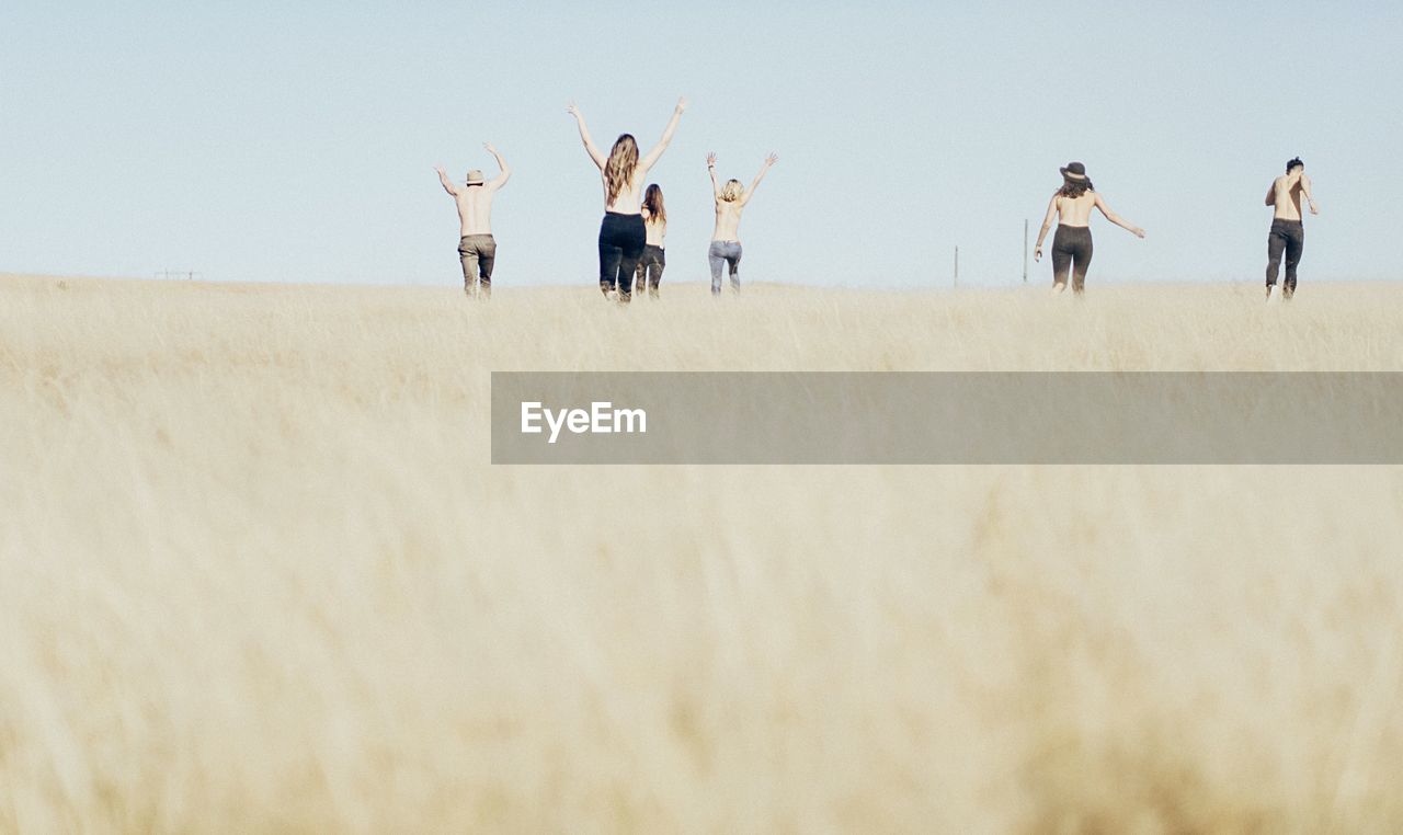 Rear view of shirtless people on landscape against clear sky