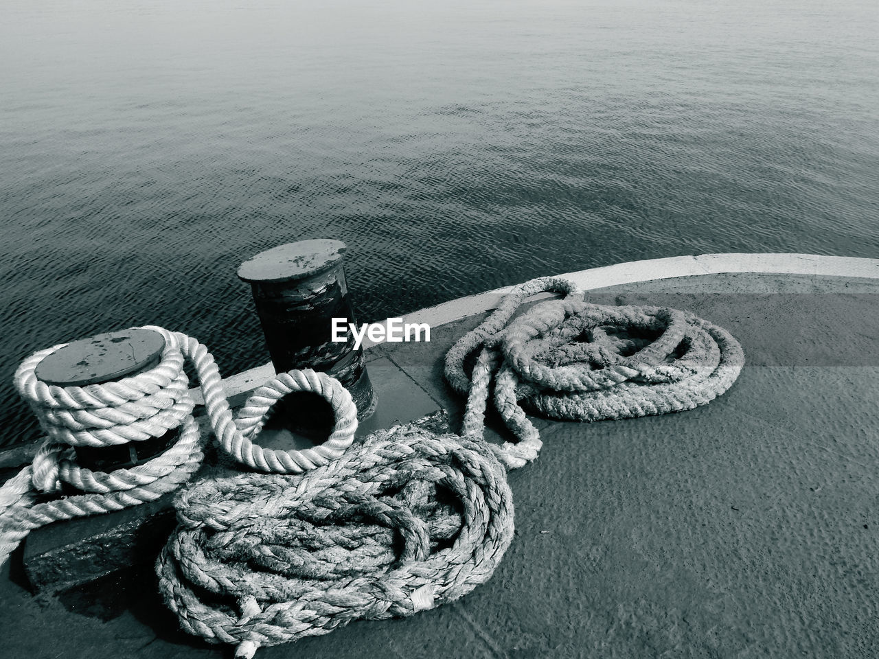 HIGH ANGLE VIEW OF ROPE TIED TO BOLLARD IN HARBOR