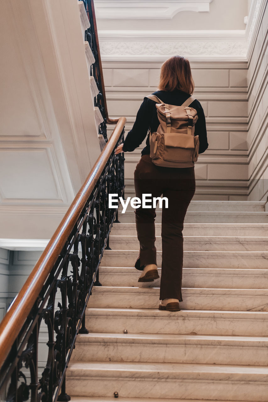 staircase, steps and staircases, stairs, one person, architecture, railing, women, adult, full length, wood, lifestyles, indoors, handrail, built structure, female, standing, young adult, hairstyle, casual clothing, rear view, clothing, looking, long hair, person