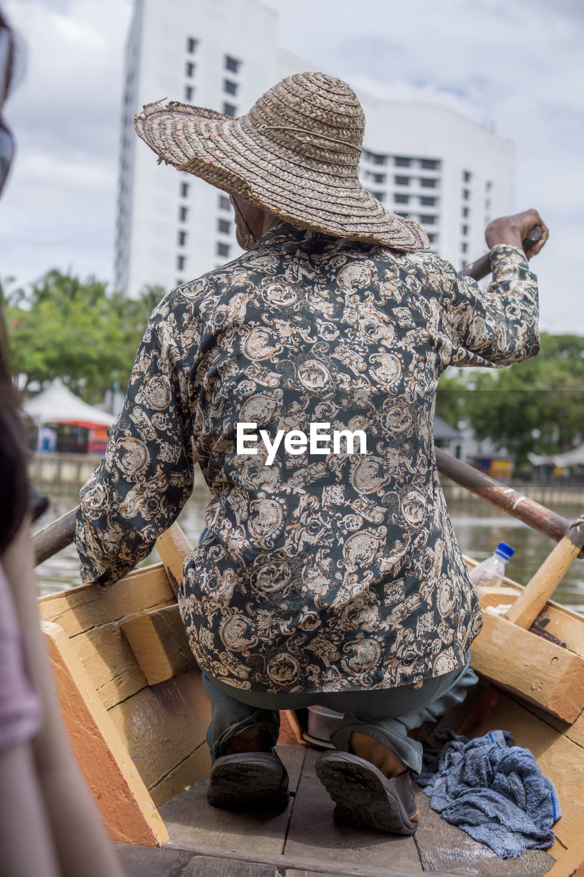 REAR VIEW OF WOMAN WEARING HAT STANDING AGAINST CITY