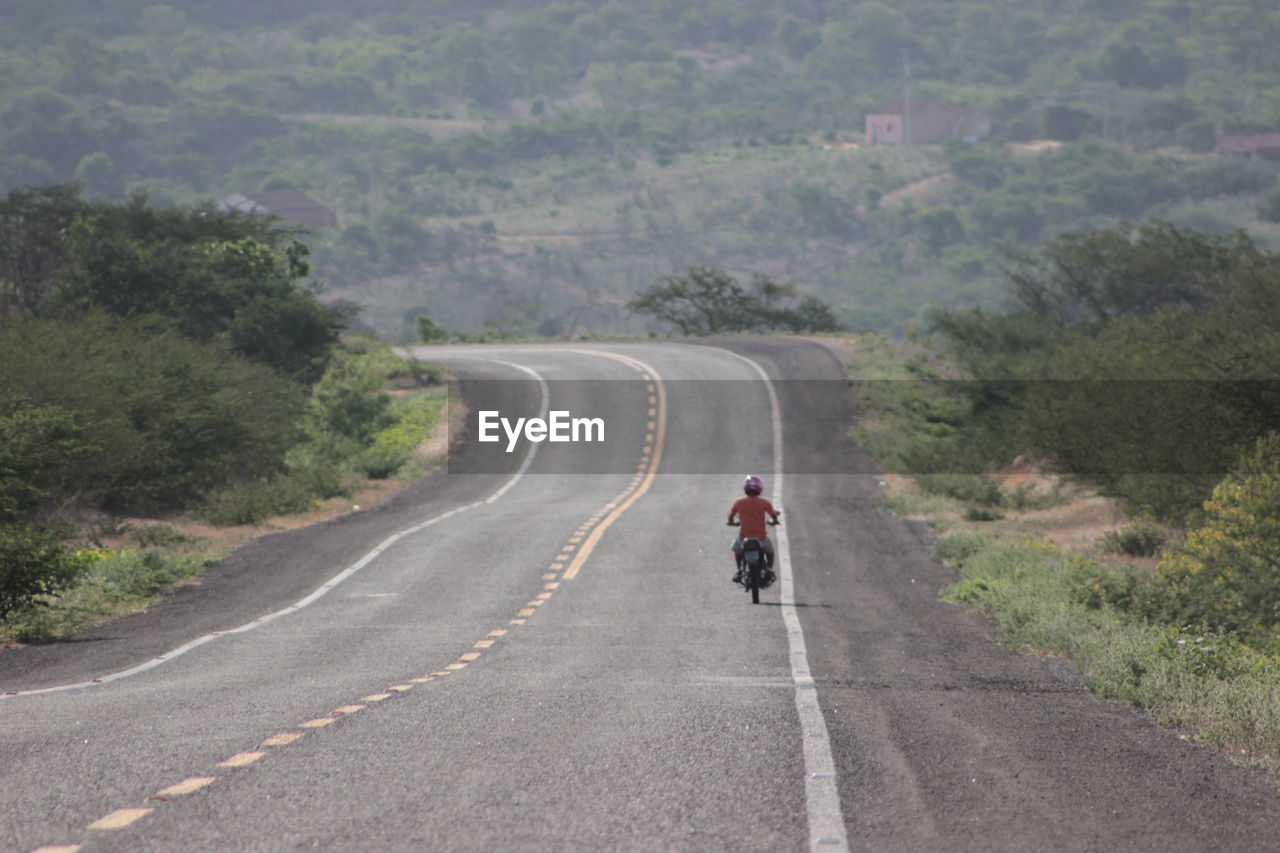 REAR VIEW OF WOMAN WALKING ON ROAD ALONG LANDSCAPE