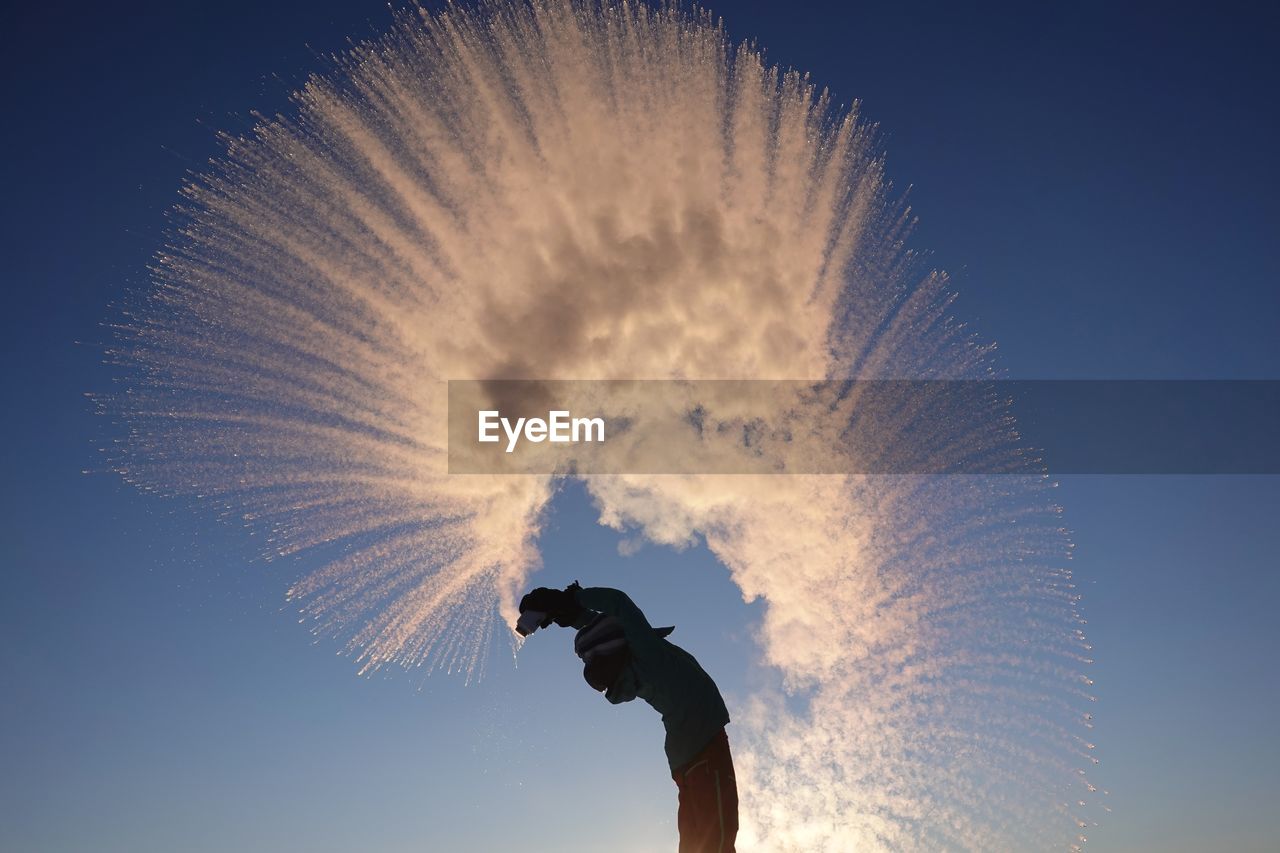 Woman throwing snow against clear blue sky