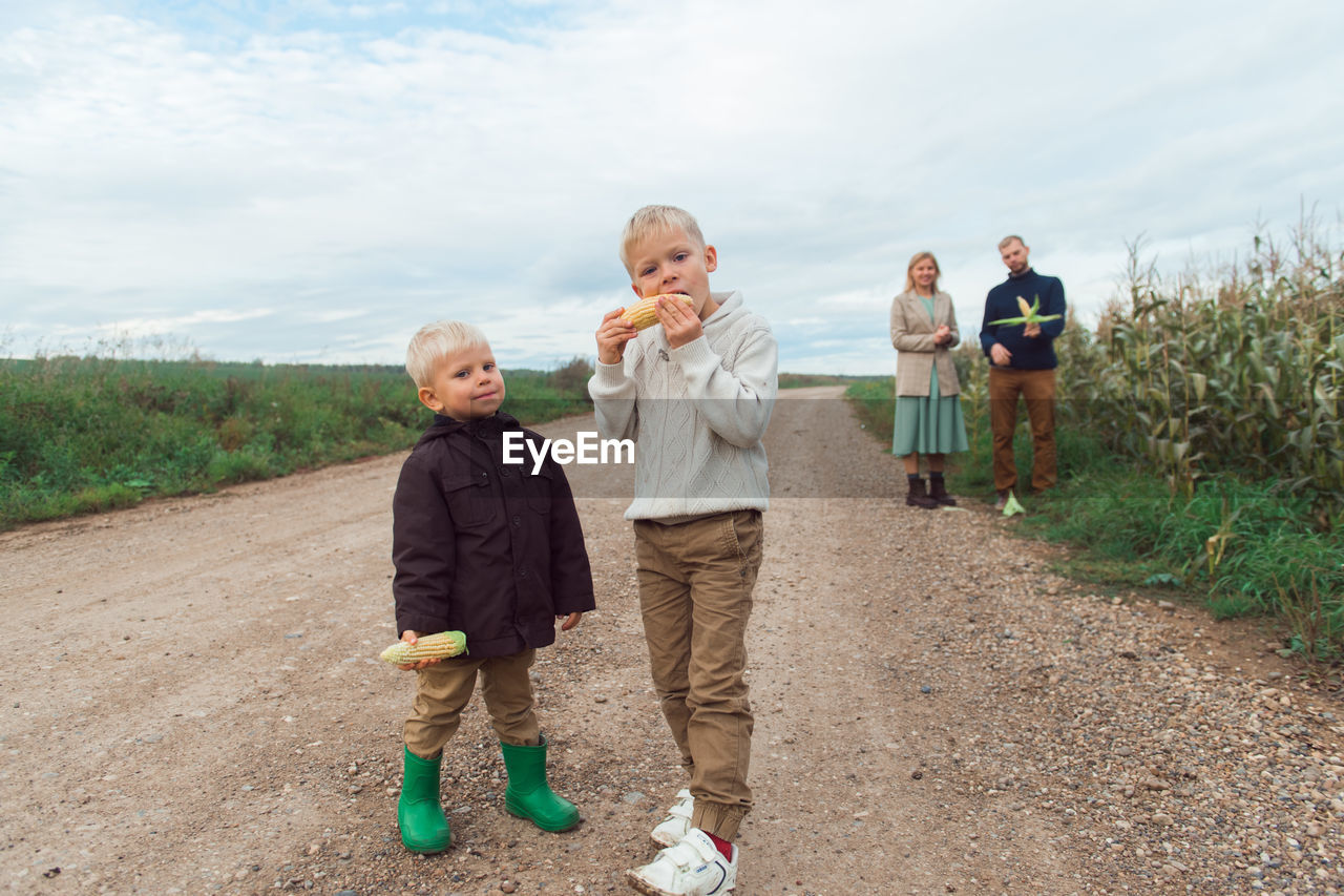 Family walking in corn field at autumn, kids eating corncob