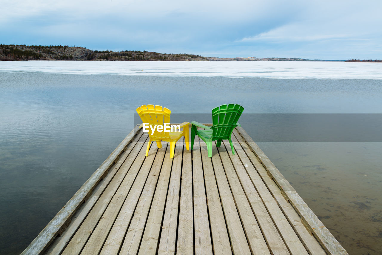 Green and yellow adirondack chairs on pier at lake during winter