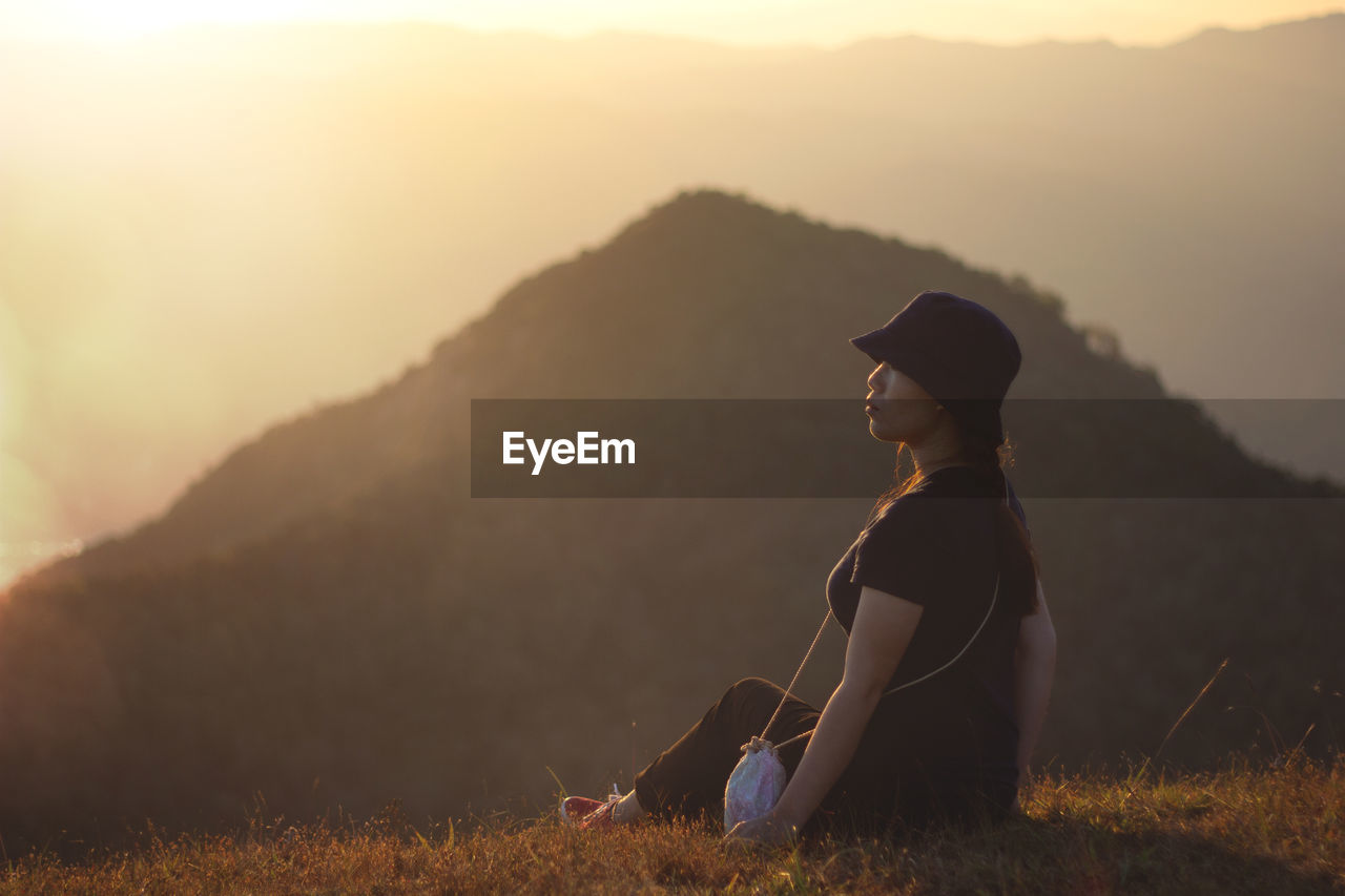 Woman looking away while sitting on mountain during sunset